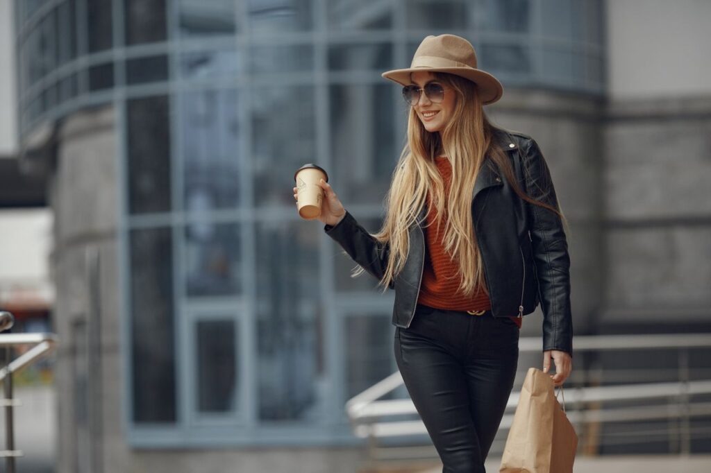 Stylish woman with coffee and shopping bag, smiling in an urban environment.